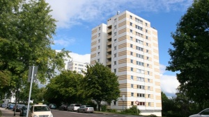 Hochhaus mit 12 Etagen an Straße, Fassade weiß und gelb. Bäume und Fahrzeuge. Hochhaus mit 12 Etagen an Straße, Fassade weiß und gelb. Bäume und Fahrzeuge.