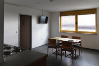 Tisch mit vier Stühlen vor Fenster, grauer PVC-Boden.