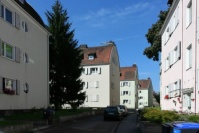 Altbauten mit Tonnendach, 4 Etagen, helle Fassaden, Klappläden, an einer Straße.