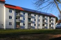 Saniertes, weißes Wohnhaus, Balkonseite, mit Wiese davor. Drei Wohnetagen. Auf dem Dach Photovoltaikanlage.