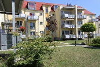 Saniertes, gelbes Wohnhaus mit Balkonen, bepflanzte Grünfläche.