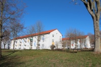 Dreigeschossige Wohnhäuser mit weißer Fassade und bunten Balkonen, vorne eine Wiese.