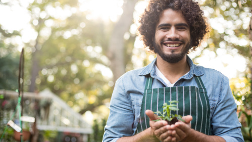 Gärtner Gärtner mit breitem Lächeln und kleiner Pflanze in der Hand