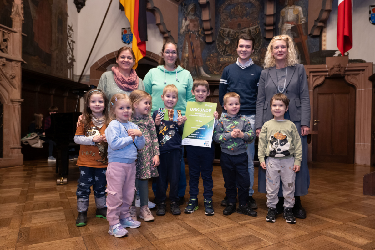 Kita Jägersfreude Preisübergabe an die Kita Jägersfreude. Zu sehen sind sieben Kinder welche die Urkunde halten und zwei Betreuerinnen der Kita, sowie zwei Jurymitglieder.