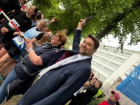 Eine Person hält eine Schreckschusspistole in Richtung Himmel, dahinter befinden sich mehrere Personen hinter einer Absperrung