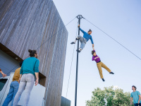 Eine Person hängt an einer großen Stange und hält eine weitere Person an der Hand fest