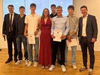 Eine Gruppe junger Menschen mit ihren Urkunden, flankiert vom zwei Männern