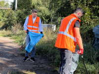 Zwei Männer in orangefarbenen Warnwesten sammeln an Gebüsch Müll auf