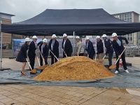 Eine Gruppe Menschen in Anzügen mit Spaten in den Händen schaufelt einen großen Haufen Sand