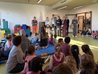 Eine Frau in einer Gruppe Erwachsener steht vor einer Kindergruppe und sagt etwas