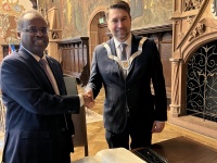 Zwei Männer stehen an einem Tisch vor einem großen Buch und reichen sich die Hand