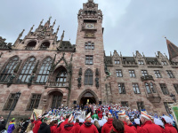 ine große Menschenmenge in Kostümen versammelt sich vor dem Saarbrücker Rathaus, das im Hintergrund vollständig zu sehen ist.