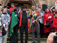 Mehrere kostümierte Personen stehen vor dem Eingang des Rathauses, während ein Mann im bunten Kostüm einen großen Schlüssel in die Höhe hält.