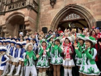 Zahlreiche kostümierte Gruppen stehen dicht gedrängt auf den Rathaustreppen, während ein Fotograf im Vordergrund ein Bild aufnimmt.