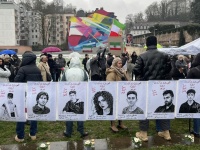 Ein langes Banner mit vielen Gesichtern wird von Demonstrierenden hochgehalten. Im Hintergrund sieht man iranische und persische Fahnen