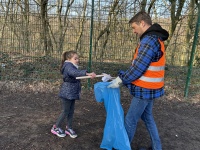 Mädchen sammelt Müll mit Greifzange, ein Erwachsener hält einen Müllsack