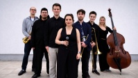 Jomila Band Sieben Musiker:innen mit Instrumenten und Mikrofonen in der Hand vor weißem Hintergrund